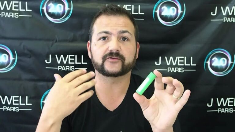 一名男子站在印有 J WELL PARIS 的背景前，手持一支綠色裝置。
